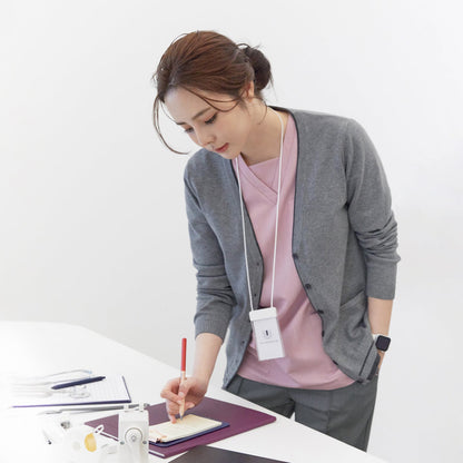 Woman wearing a gray soft touch cardigan over a pink top and gray pants, writing on a notepad at a desk, with a lanyard around her neck and smartwatch on her wrist,Gray