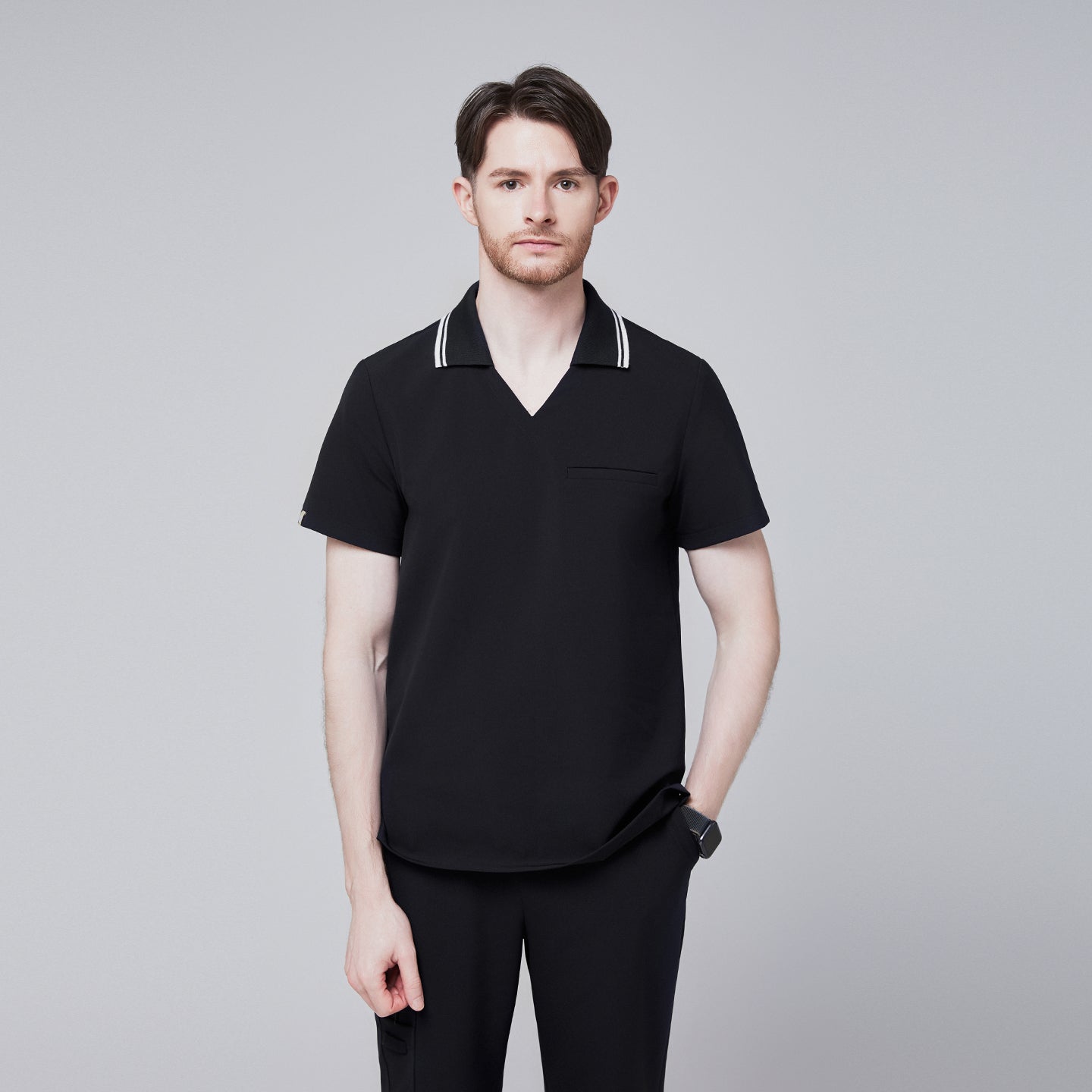 Male model wearing a jet black performance polo scrub top with a striped collar and matching pants, standing with one hand in pocket,Jet Black