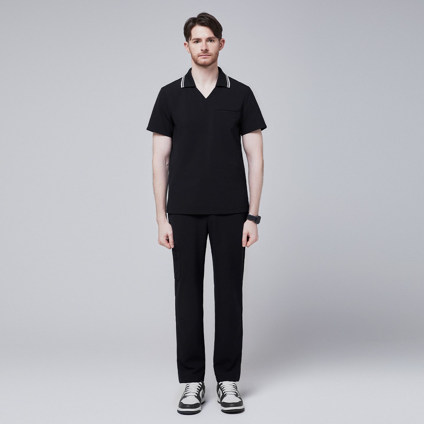 Male model wearing a jet black performance polo scrub top with a striped collar and matching pants, standing straight with sneakers,Jet Black