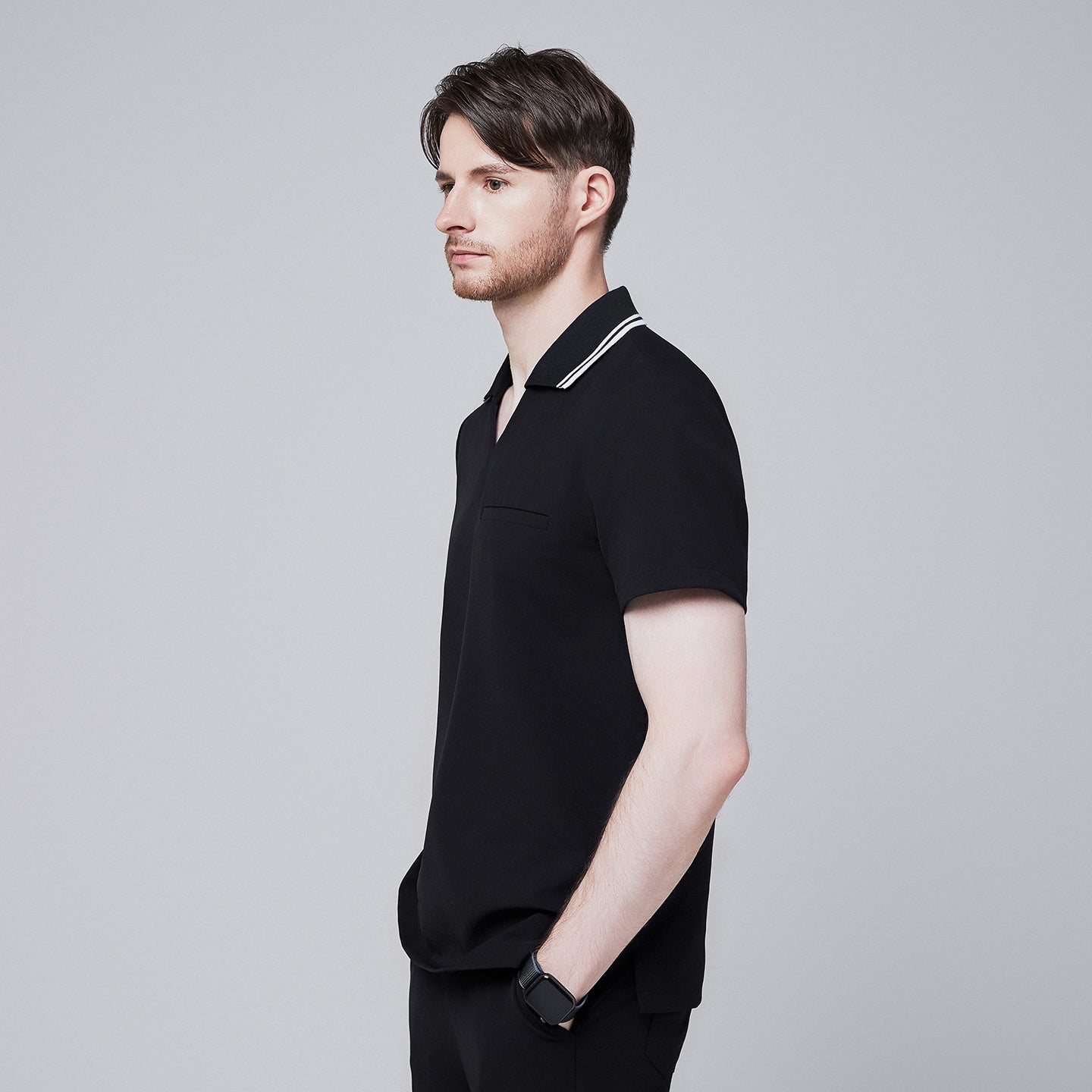 Side profile of a male model wearing a jet black performance polo scrub top with a striped collar and hands in pockets,Jet Black