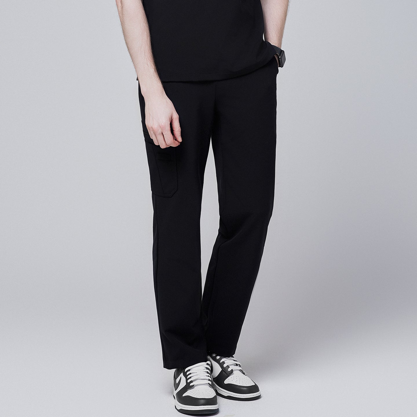 Male model wearing jet black relaxed-fit scrub pants with side pocket detailing, standing with one hand in pocket, showcasing a casual and polished look,Jet Black