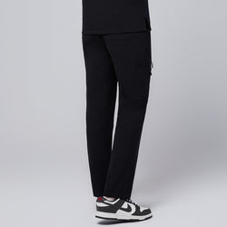 Image of Male model wearing jet black relaxed-fit scrub pants featuring a rear view of the functional side pocket design, paired with black and white sneakers for a professional appearance,Jet Black