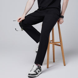 Image of Male model sitting on a wooden stool wearing jet black relaxed-fit scrub pants paired with black and white sneakers, holding a pair of sunglasses for a casual yet professional look,Jet Black