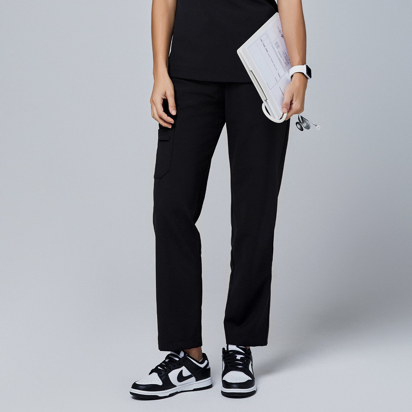 Black utility scrub pants with functional side pockets, worn with a black top and paired with black-and-white sneakers, holding a clipboard and stethoscope,Jet Black