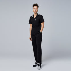 Image of Female model wearing a jet black essential polo scrub top with a striped collar and matching pants, accessorized with safety glasses and sneakers,Jet Black