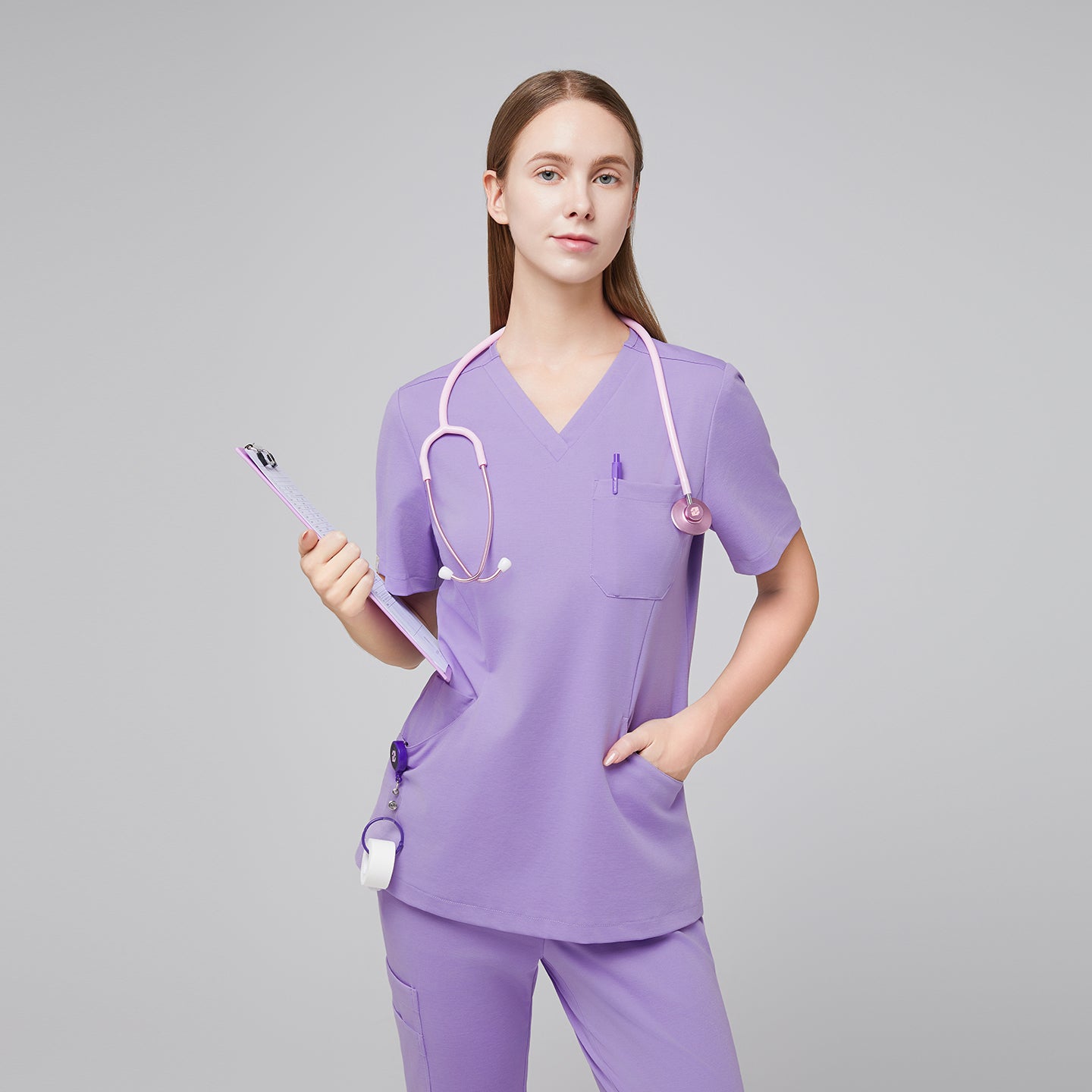 Front view of a woman wearing a lavender scrub top and pants, accessorized with a pink stethoscope and holding a clipboard, highlighting a stylish and functional medical uniform,Lavender