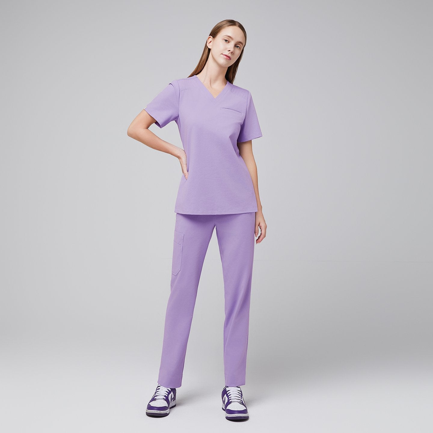 A woman wearing a Lavender Pleated Shoulder Scrub Top and Lavender Straight Split Hem Scrub Pants, standing in a relaxed pose,Lavender