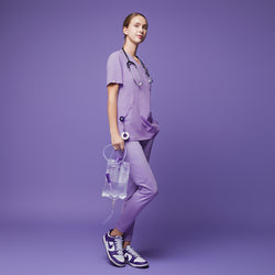 Image of Woman dressed in a lavender scrub set, holding a medical fluid bag, standing confidently against a matching lavender backdrop,Lavender