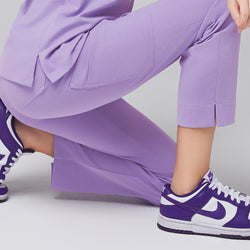 Image of Close-up of lavender scrub pants with split hem detail, shown while kneeling, paired with purple sneakers,Lavender