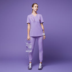 Image of Female wearing lavender jogger scrub pants and top with a stethoscope, holding a medical fluid bag, paired with purple and white sneakers,Lavender