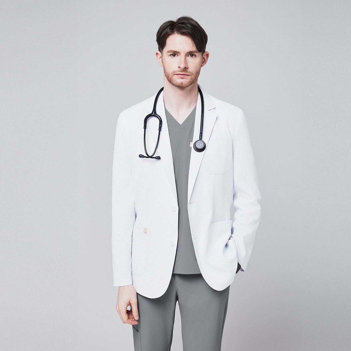 A man wearing a short white lab coat (LCM-01) over an Ash Gray Single Pocket Scrub Top and Ash Gray StretchFit Jogger Scrub Pants, with a stethoscope around his neck,White