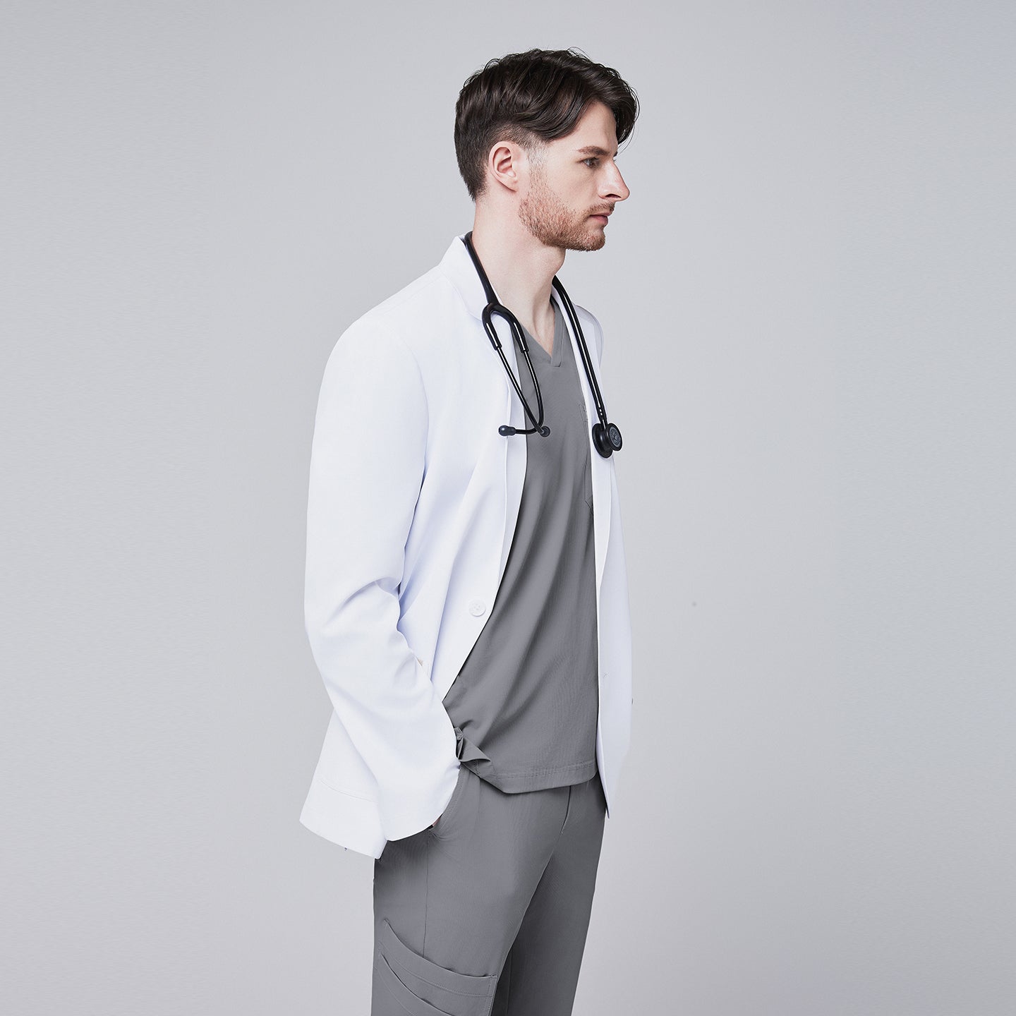 Side view of a man wearing a short white lab coat (LCM-01) over an Ash Gray Single Pocket Scrub Top and Ash Gray StretchFit Jogger Scrub Pants, with his hand in his pocket,White