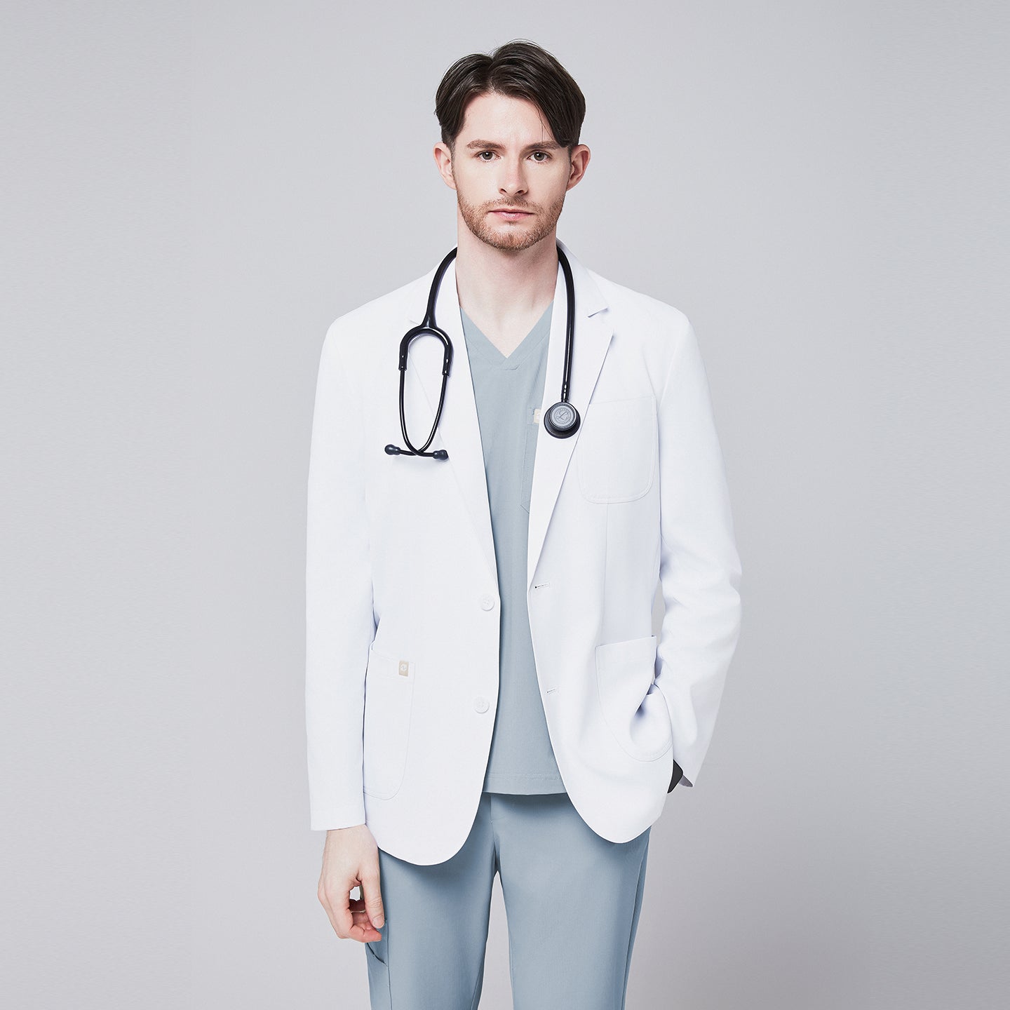 A man wearing a short white lab coat (LCM-01) over a Cool Gray Single Pocket Scrub Top and Cool Gray StretchFit Jogger Scrub Pants, with a stethoscope around his neck,White