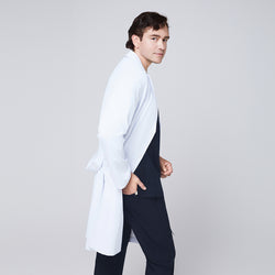 Image of Side view of a man wearing a long white lab coat (LCM-02) over an Eco Navy Double Pocket Scrub Top and Eco Navy Zipper Pocket Straight Scrub Pants, looking toward the camera,Eco Navy