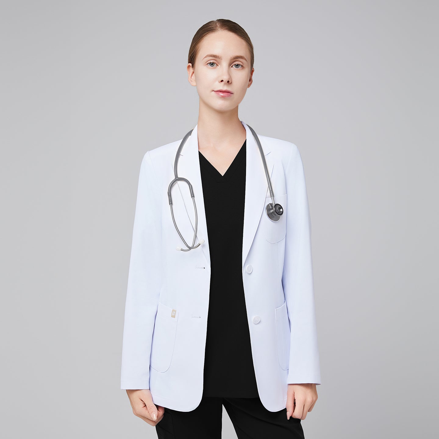 A woman wearing a short white lab coat (LCW-02) over an Eco Black Double Pocket Scrub Top and Eco Black Zipper Pocket Jogger Scrub Pants, with a stethoscope around her neck,White