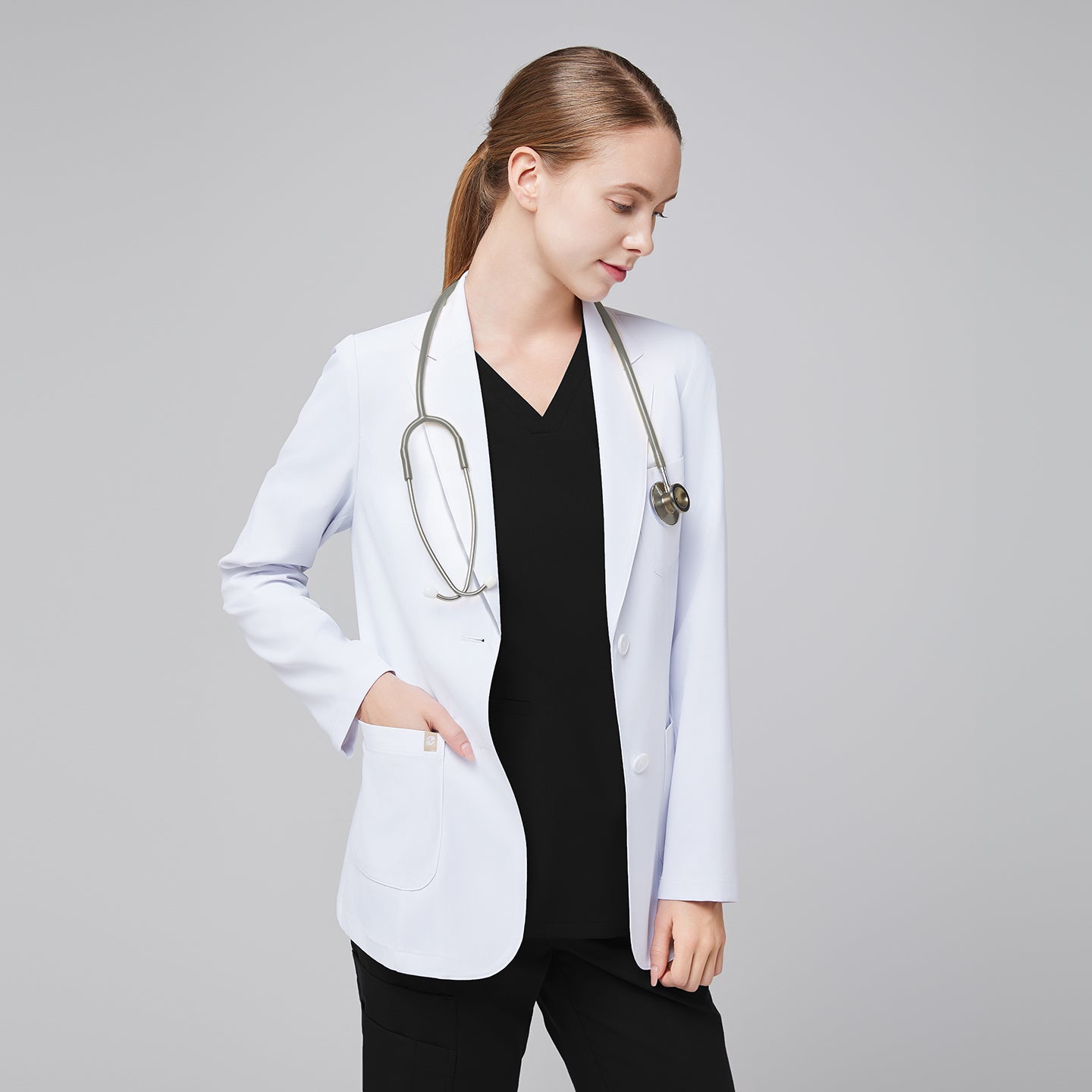 A woman wearing a short white lab coat (LCW-02) over an Eco Black Double Pocket Scrub Top and Eco Black Zipper Pocket Jogger Scrub Pants, placing her hand in the lab coat pocket,White