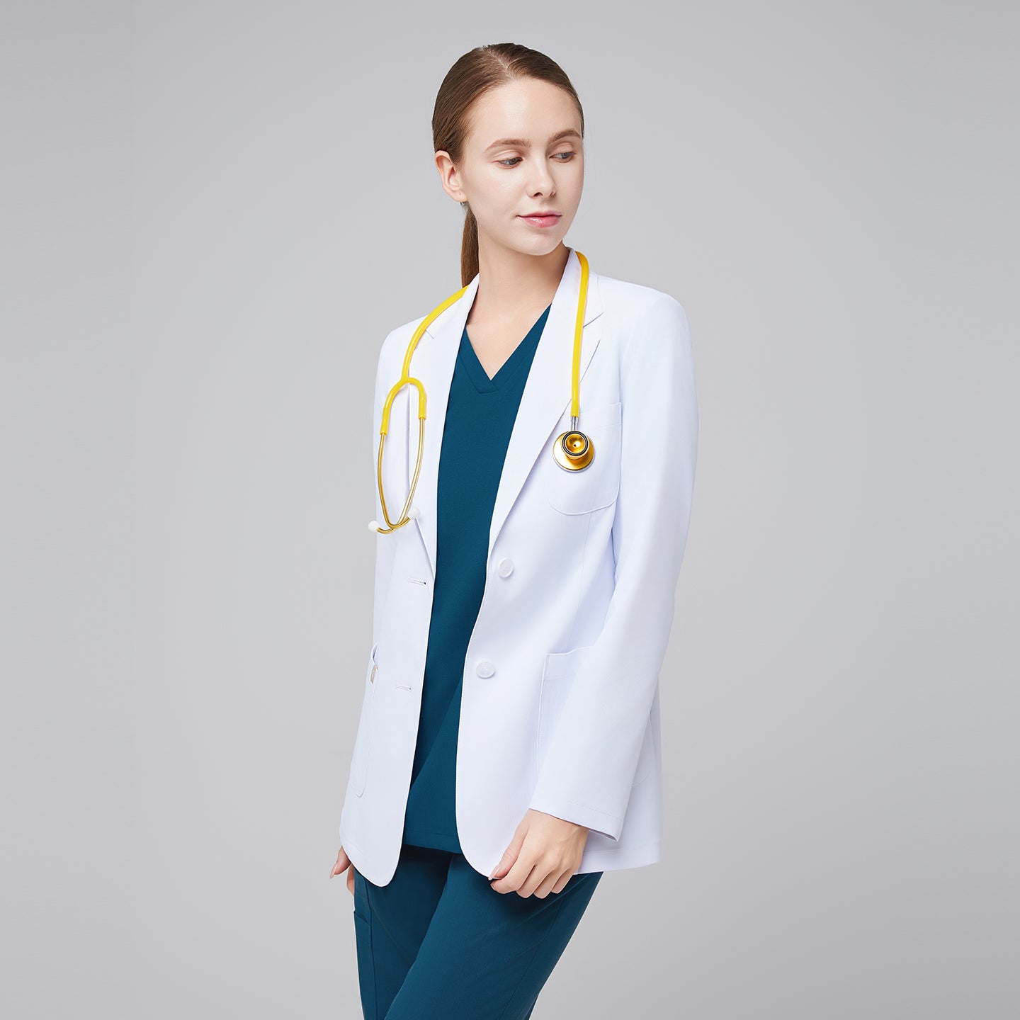 A woman wearing a short white lab coat (LCW-02) over an Ocean Teal Double Pocket Scrub Top and Ocean Teal StretchFit Jogger Scrub Pants, looking to the side while holding a yellow stethoscope,White