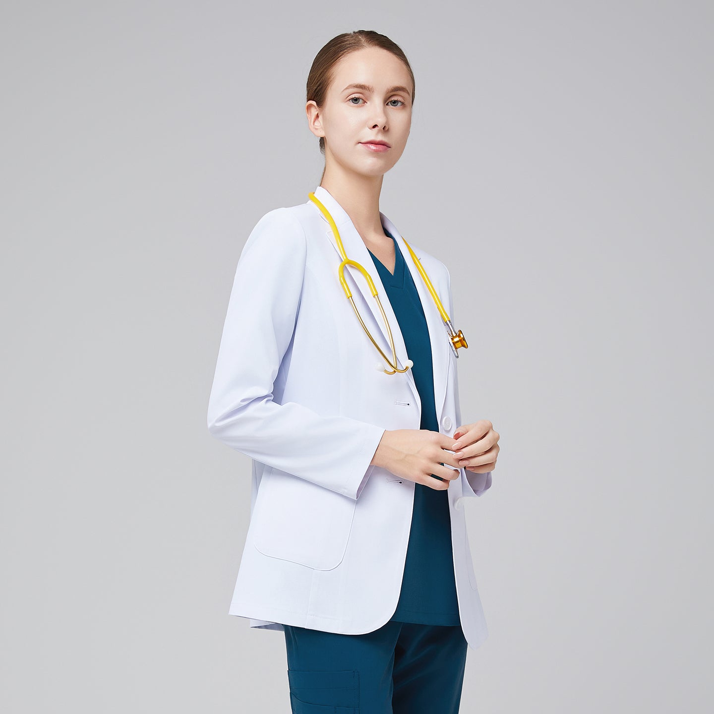 A woman wearing a short white lab coat (LCW-02) over an Ocean Teal Double Pocket Scrub Top and Ocean Teal StretchFit Jogger Scrub Pants, holding a yellow stethoscope,White