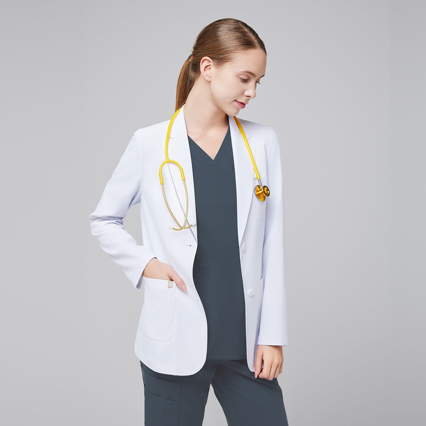 A woman wearing a short white lab coat (LCW-02) over a Smoky Blue Double Pocket Scrub Top and Smoky Blue Straight Split Hem Scrub Pants, with a yellow stethoscope around her neck,White