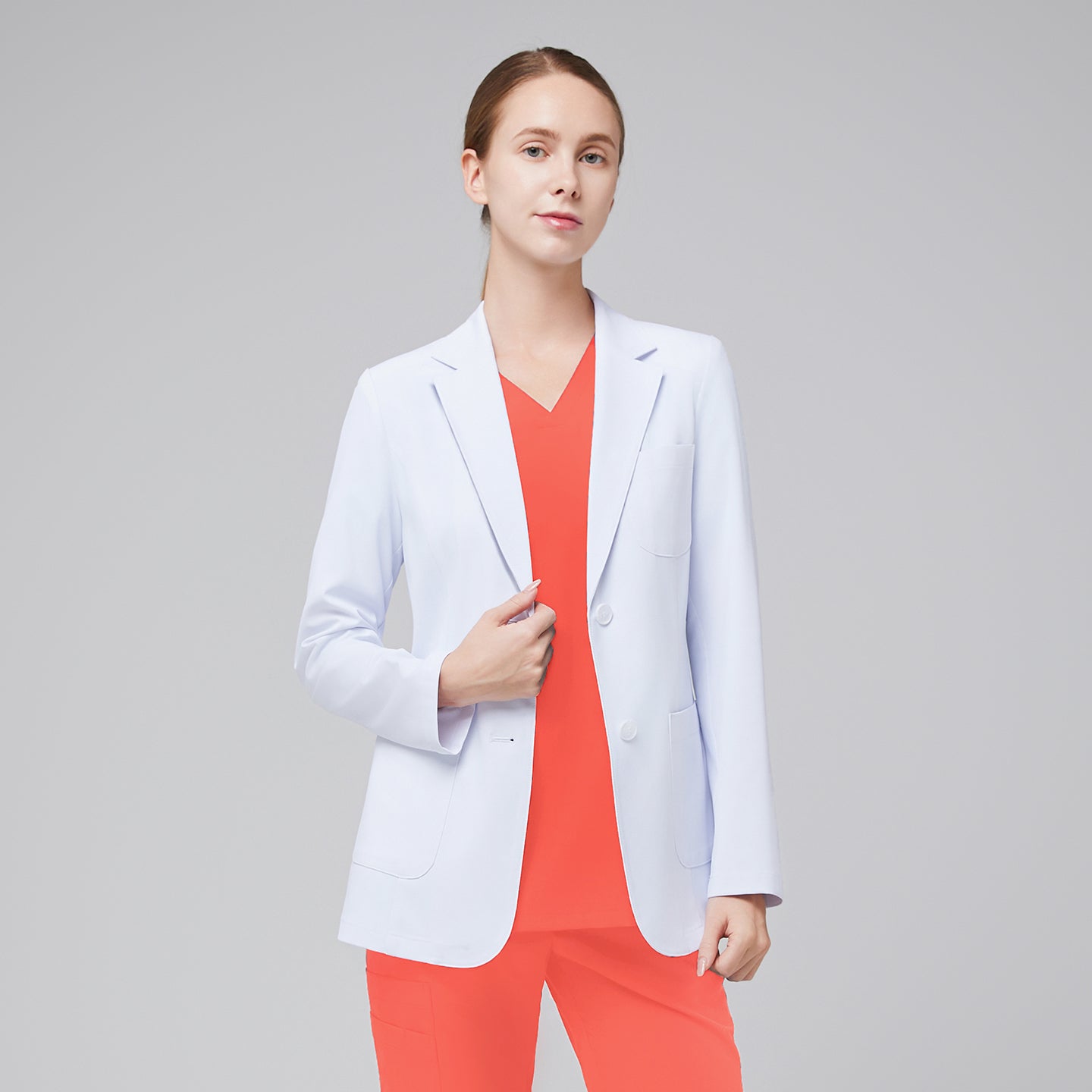 A woman wearing a short white lab coat (LCW-02) over a Tiger Orange Double Pocket Scrub Top and Tiger Orange Straight Split Hem Scrub Pants,White