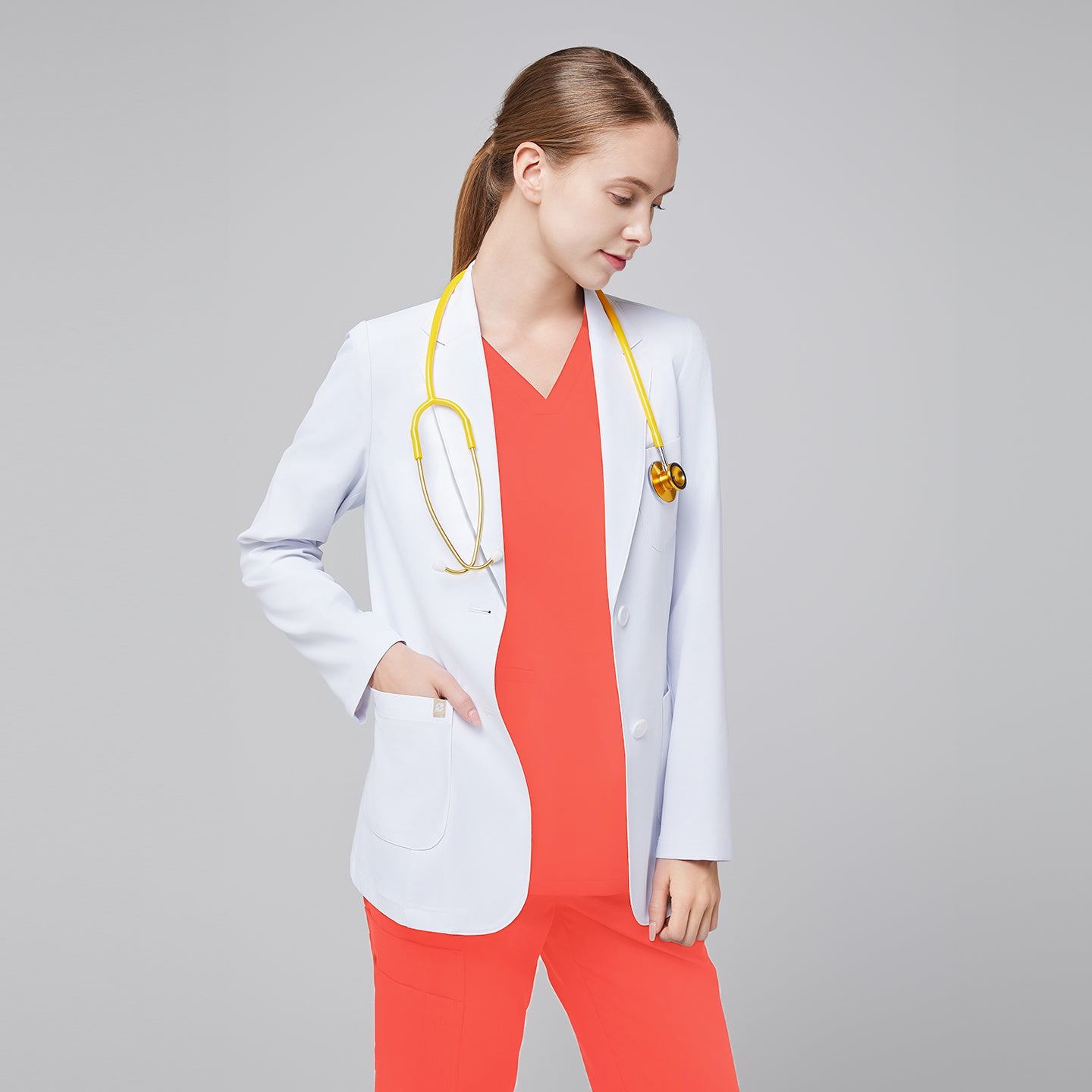 A woman wearing a short white lab coat (LCW-02) over a Tiger Orange Double Pocket Scrub Top and Tiger Orange Straight Split Hem Scrub Pants, with a yellow stethoscope around her neck,White