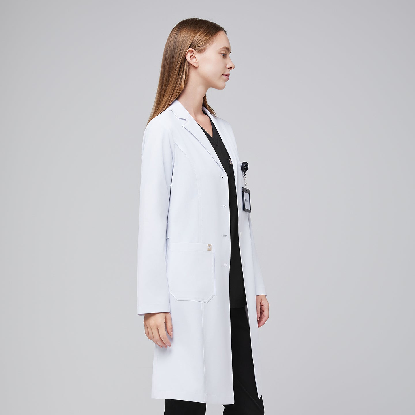 Side view of a woman wearing a long white lab coat (LCW-04) over a Midnight Black Single Pocket Scrub Top and Midnight Black Zipper Pocket Jogger Scrub Pants,White