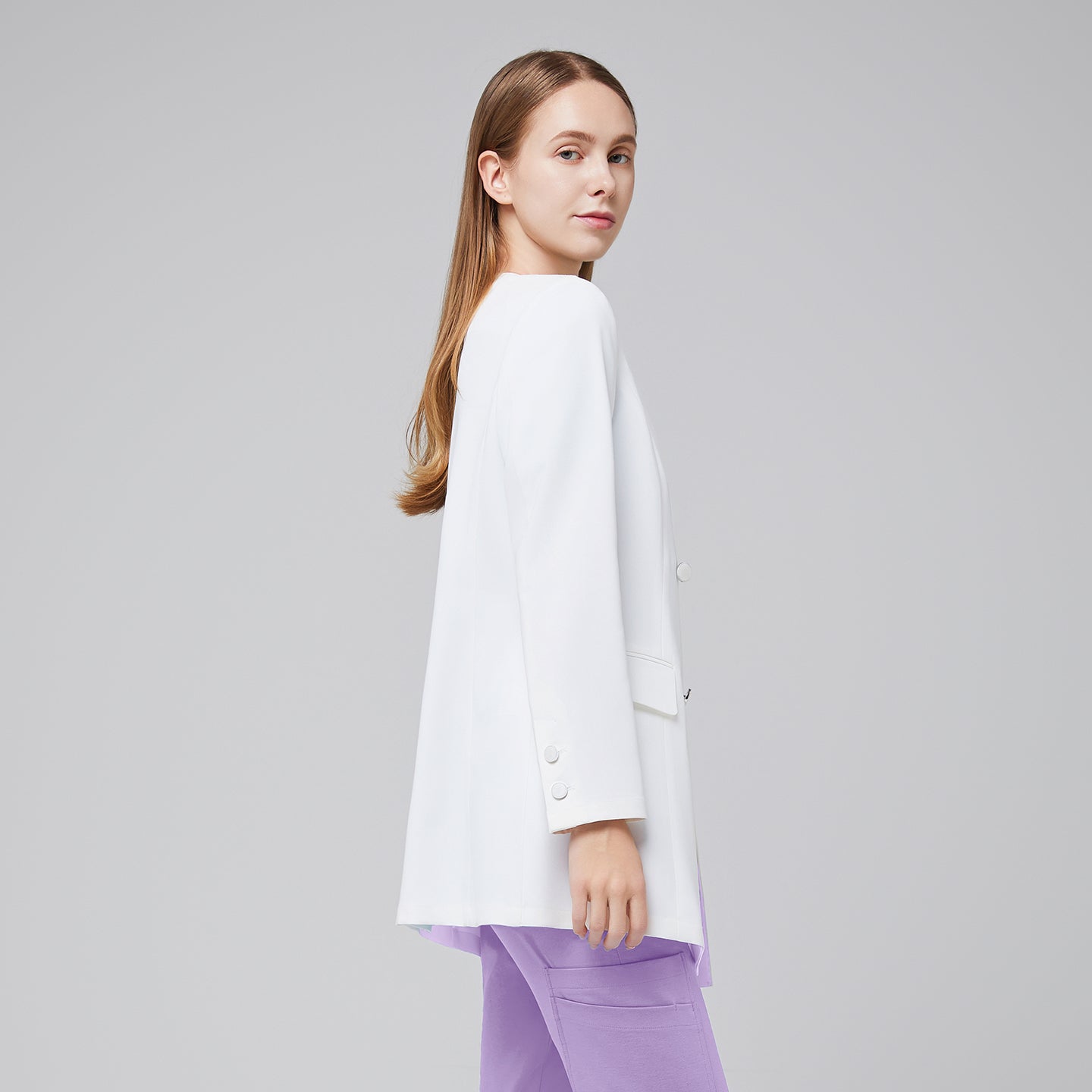 Side view of a woman wearing a white long lab coat (LCW-09) over a Lavender Pleated Shoulder Scrub Top and Lavender Straight Split Hem Scrub Pants,White