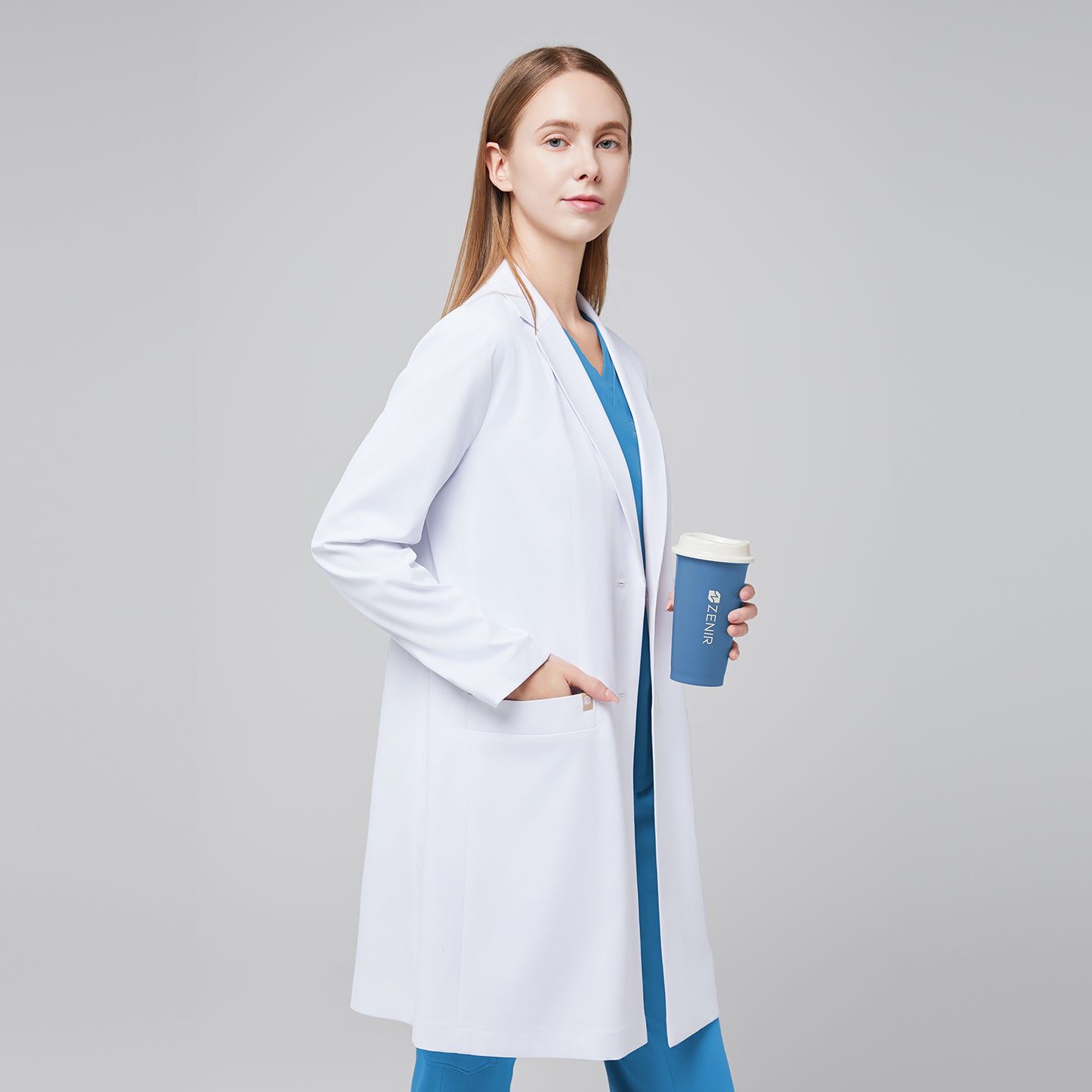 A woman wearing a white long lab coat (LCW-10) over an Aqua Blue Soft Stretch Scrub Top and Aqua Blue Straight Split Hem Scrub Pants, holding a coffee cup,White






