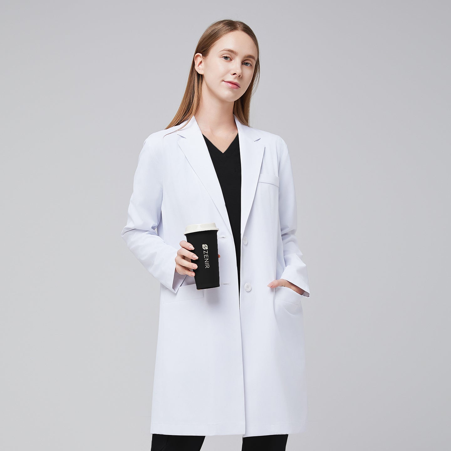 A woman wearing a white long lab coat (LCW-10) over a black scrub top and pants, holding a coffee cup,White






