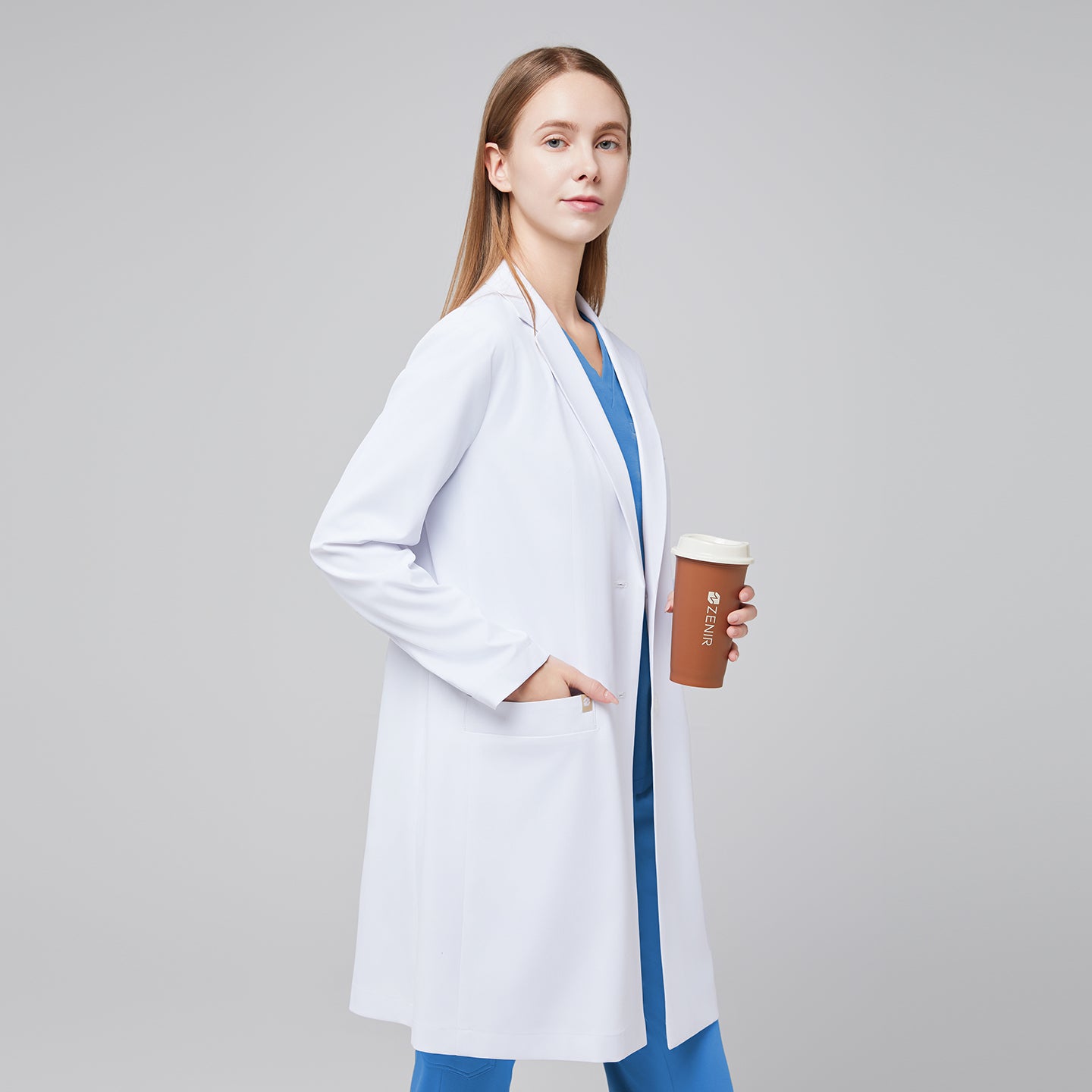 A woman wearing a white long lab coat (LCW-10) over a sky blue scrub top and pants, holding a coffee cup,White





,White