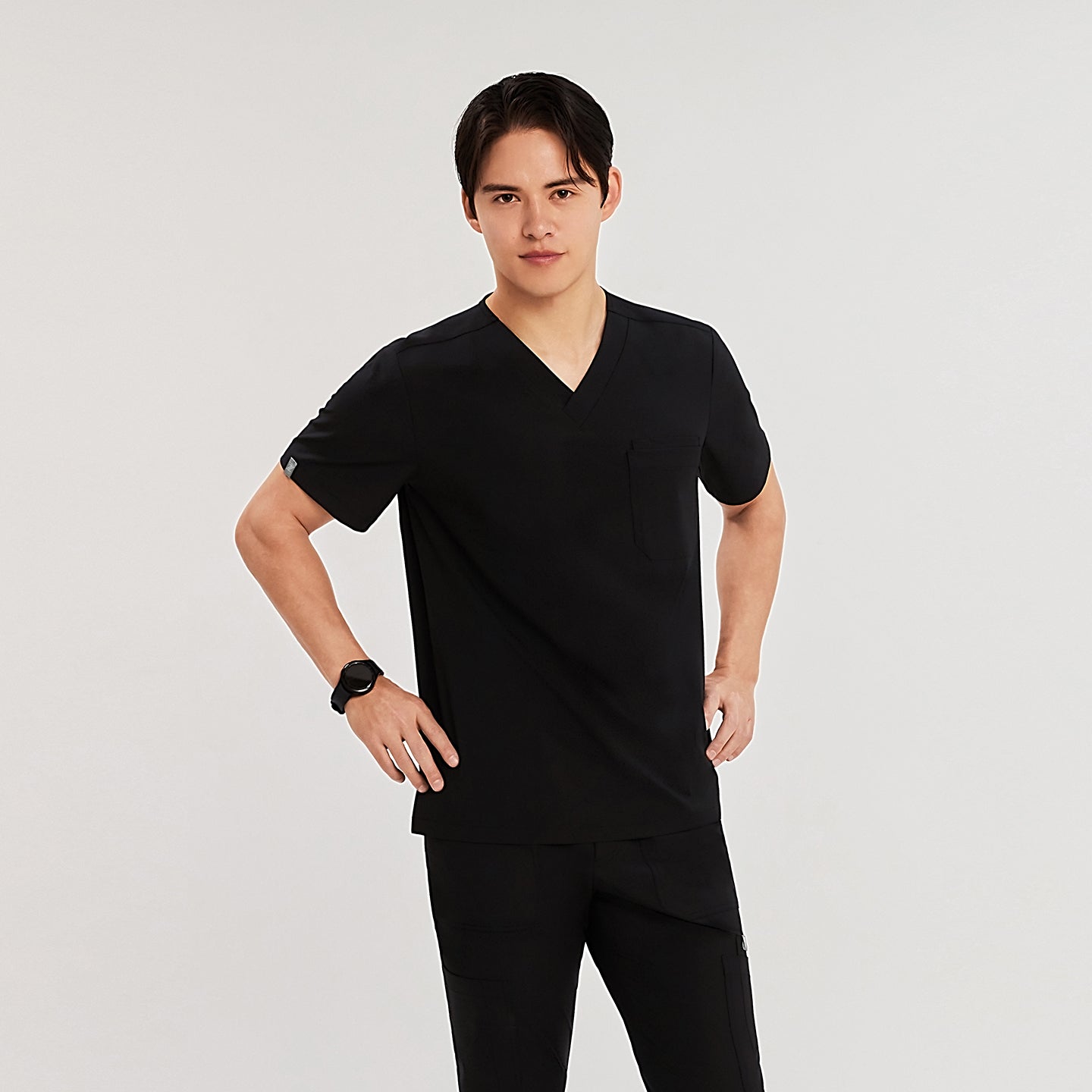 Man in black Zenir scrub top with chest pocket, standing with hands on hips, looking at the camera,Black