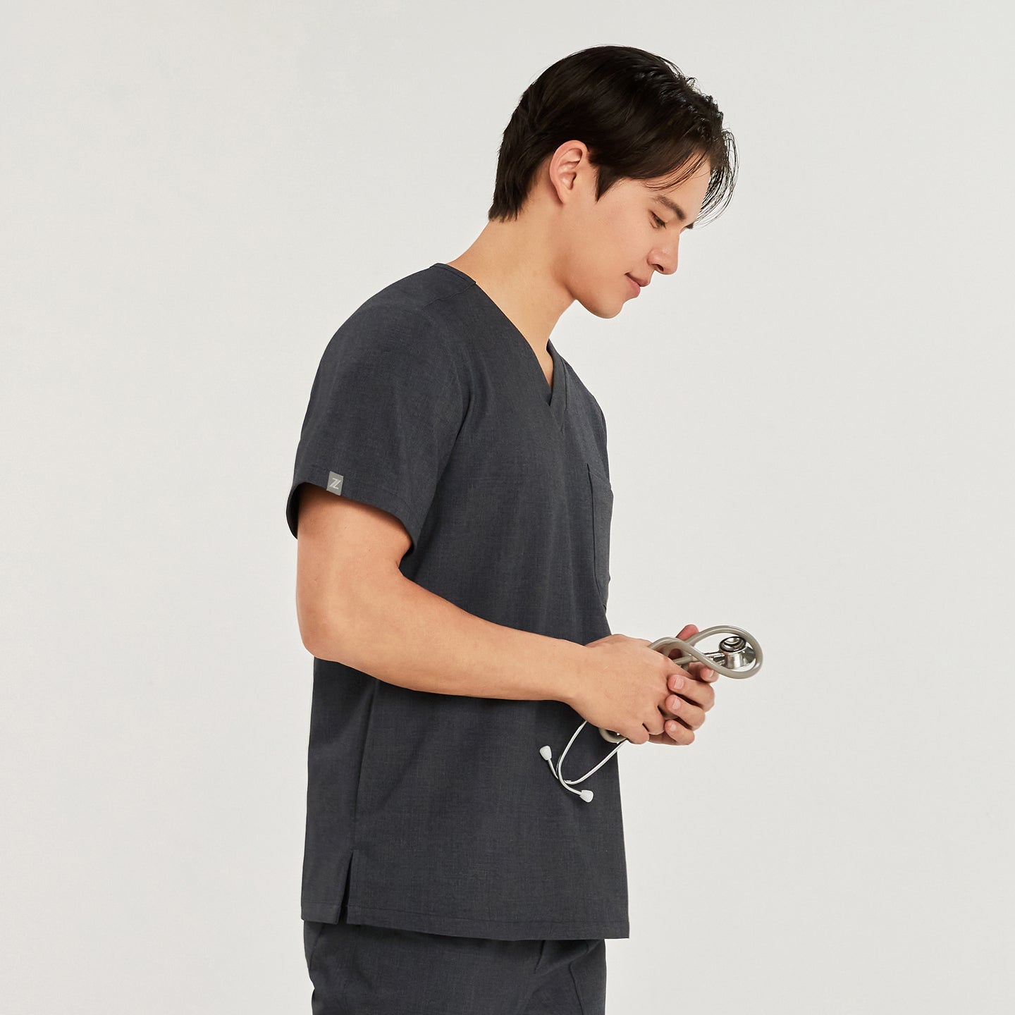 A man wearing a 3-pocket scrub top, shown from the side, holding a stethoscope,Charcoal Gray