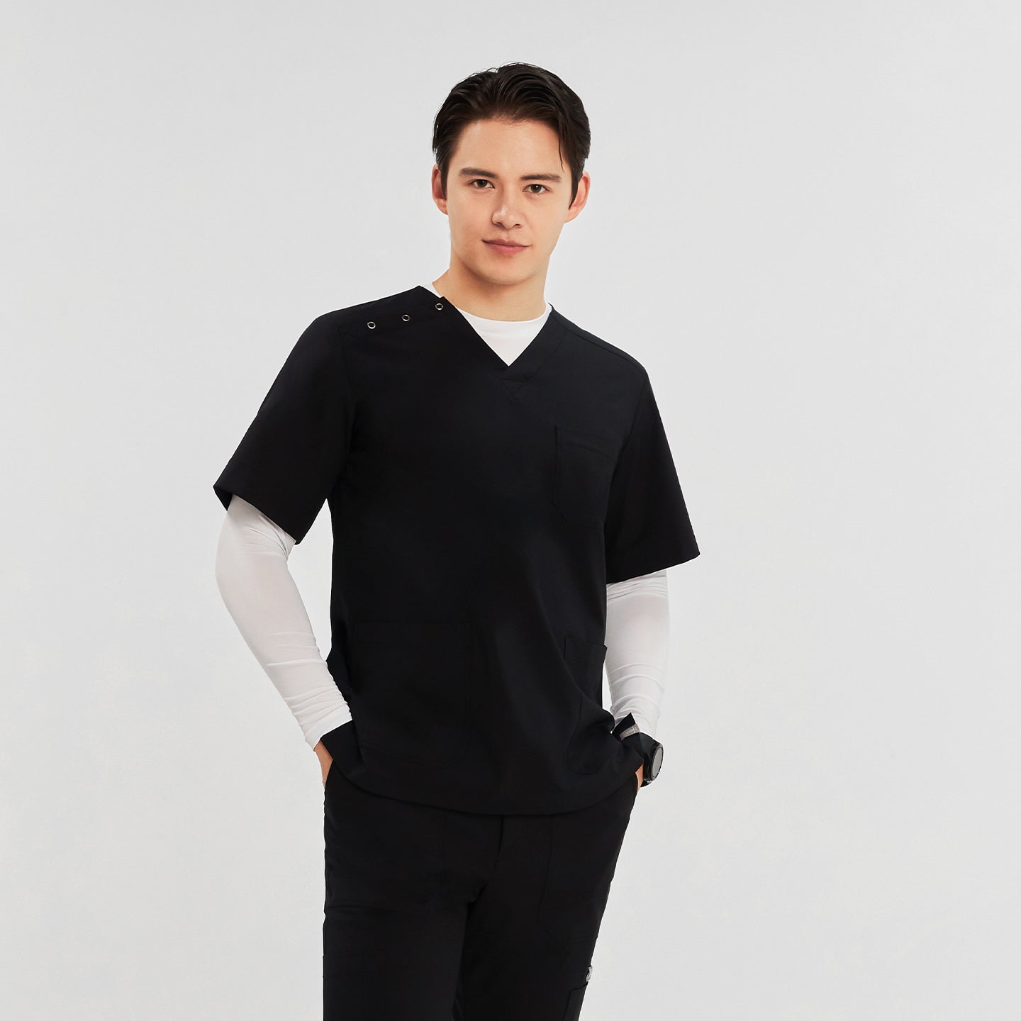  A man wearing a short-sleeved, V-neck scrub top with three buttons on the shoulder, white long sleeves underneath, and matching pants,Black