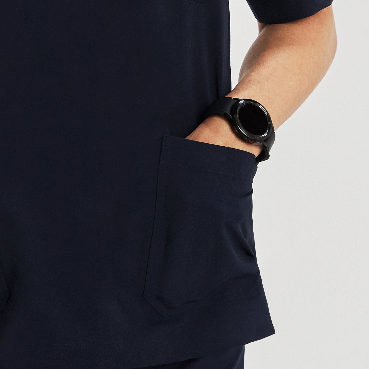 Close-up view of a man wearing a scrub top, focusing on the pocket detail with his hand inside the pocket and a smartwatch on his wrist,Navy
