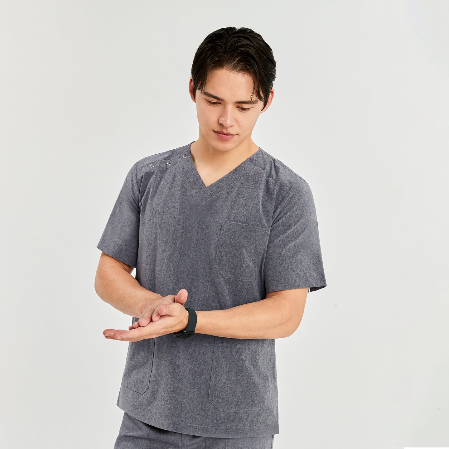 A man wearing a soft gray scrub top, standing and rubbing his hands together against a plain background,Soft Gray