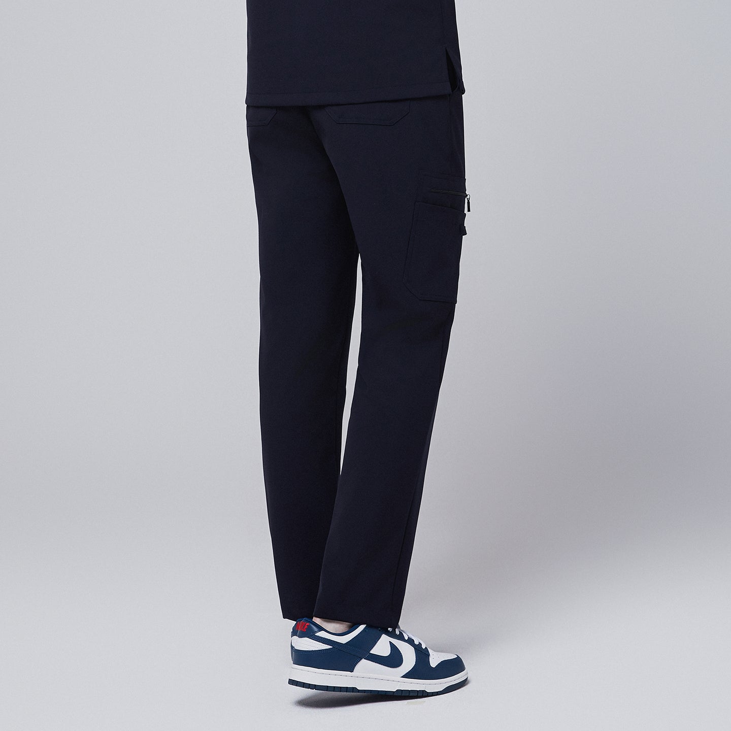 Male model showcasing the back view of midnight navy relaxed-fit scrub pants with a side pocket, emphasizing the details of the rear and side design, against a plain background,Midnigh Navy