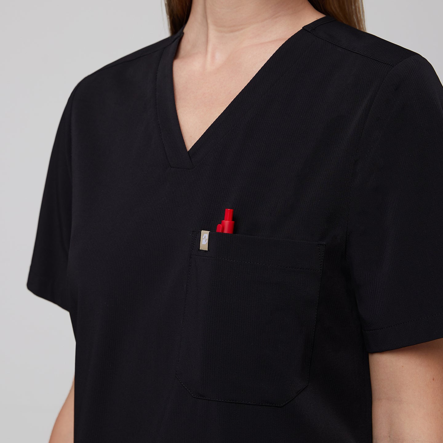 Close-up of a midnight black scrub top's single pocket holding a red pen, highlighting the fabric texture and design details,Midnight Black