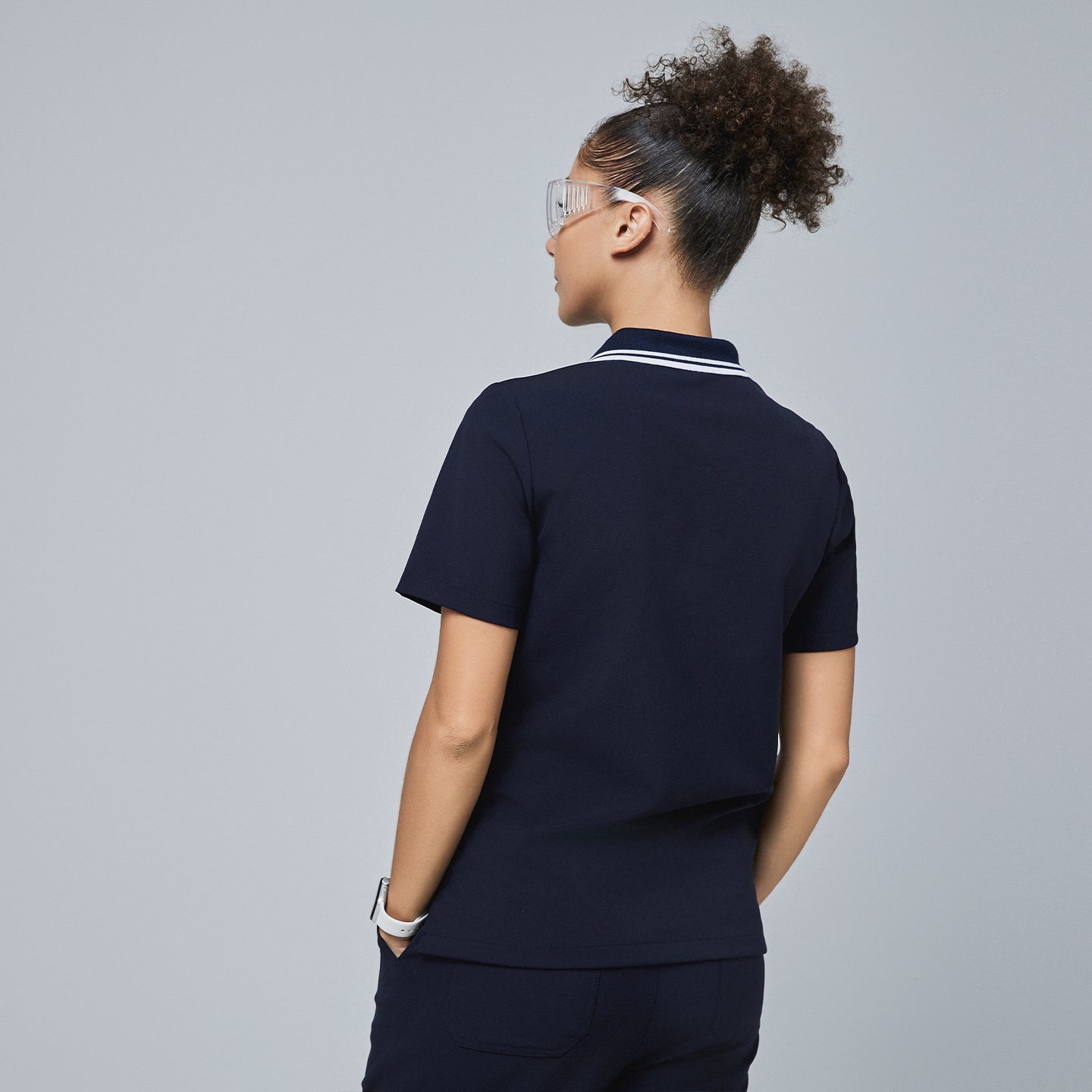 Back view of a woman wearing a navy blue polo scrub top with a white striped collar and matching navy scrub pants,Midnight Navy