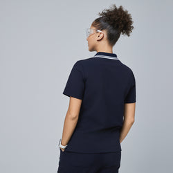 Image of Back view of a woman wearing a navy blue polo scrub top with a white striped collar and matching navy scrub pants,Midnight Navy