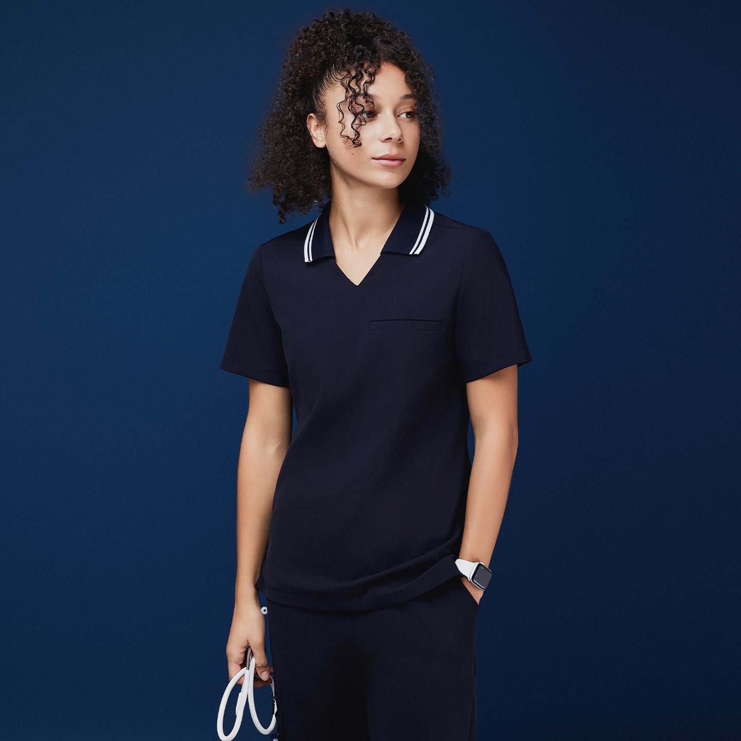 Woman wearing a navy blue polo scrub top with a white striped collar, holding a stethoscope, paired with matching navy pants,Midnight Navy