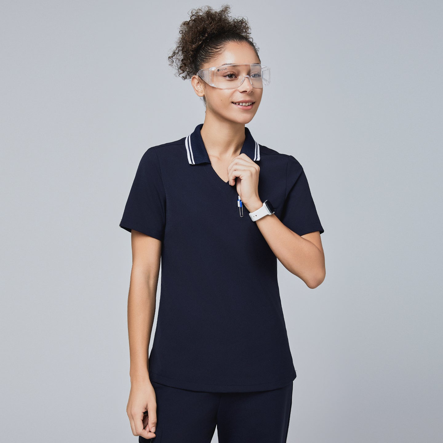 Woman wearing a navy blue polo scrub top with a white striped collar, holding the collar, paired with matching navy pants,Midnight Navy