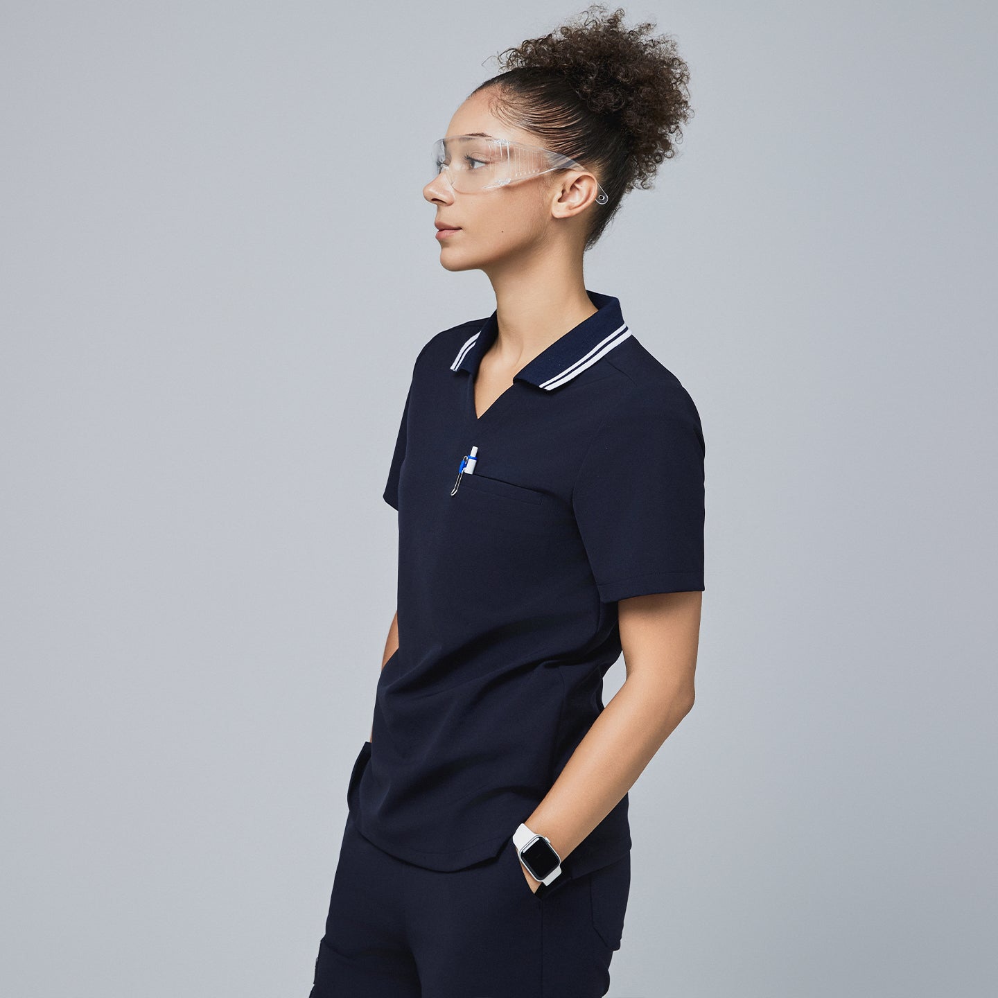 Woman in a navy blue polo scrub top with white striped collar and matching pants, holding a pen in the chest pocket,Midnight Navy