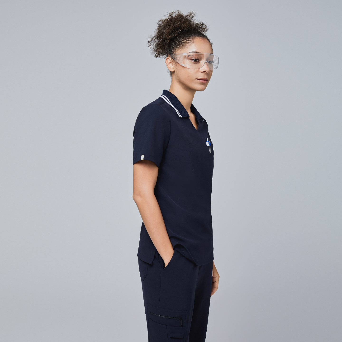 Side view of a woman wearing a navy blue polo scrub top with a white striped collar and matching navy scrub pants,Midnight Navy