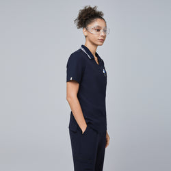 Image of Side view of a woman wearing a navy blue polo scrub top with a white striped collar and matching navy scrub pants,Midnight Navy