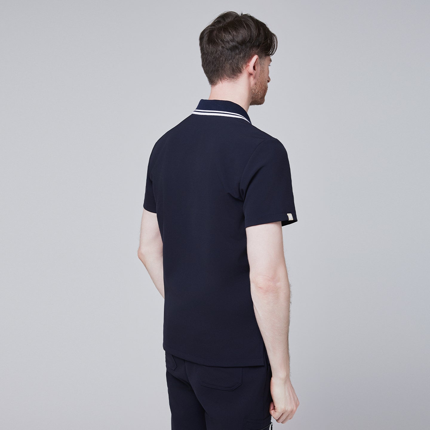 Male model wearing a midnight navy performance polo scrub top with a striped collar, viewed from behind,Midnight Navy