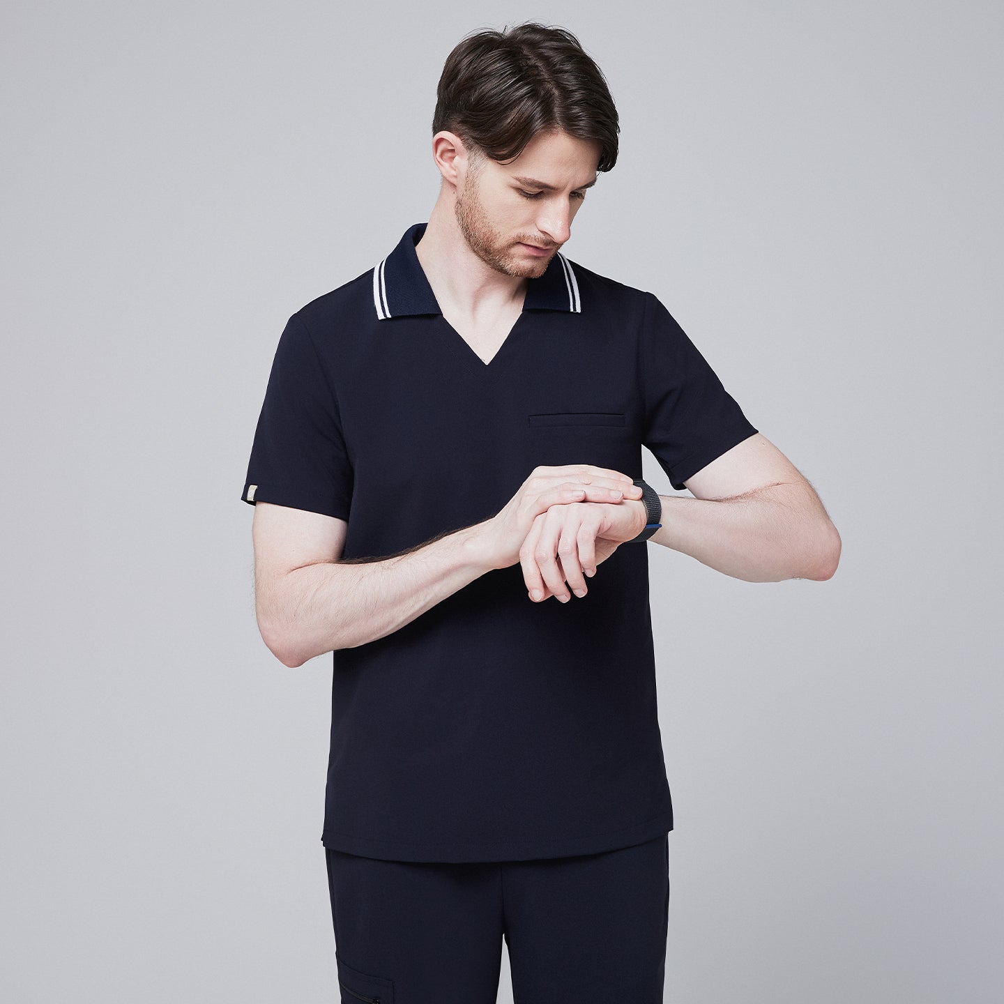 Male model wearing a midnight navy performance polo scrub top with a striped collar, checking a smartwatch,Midnight Navy