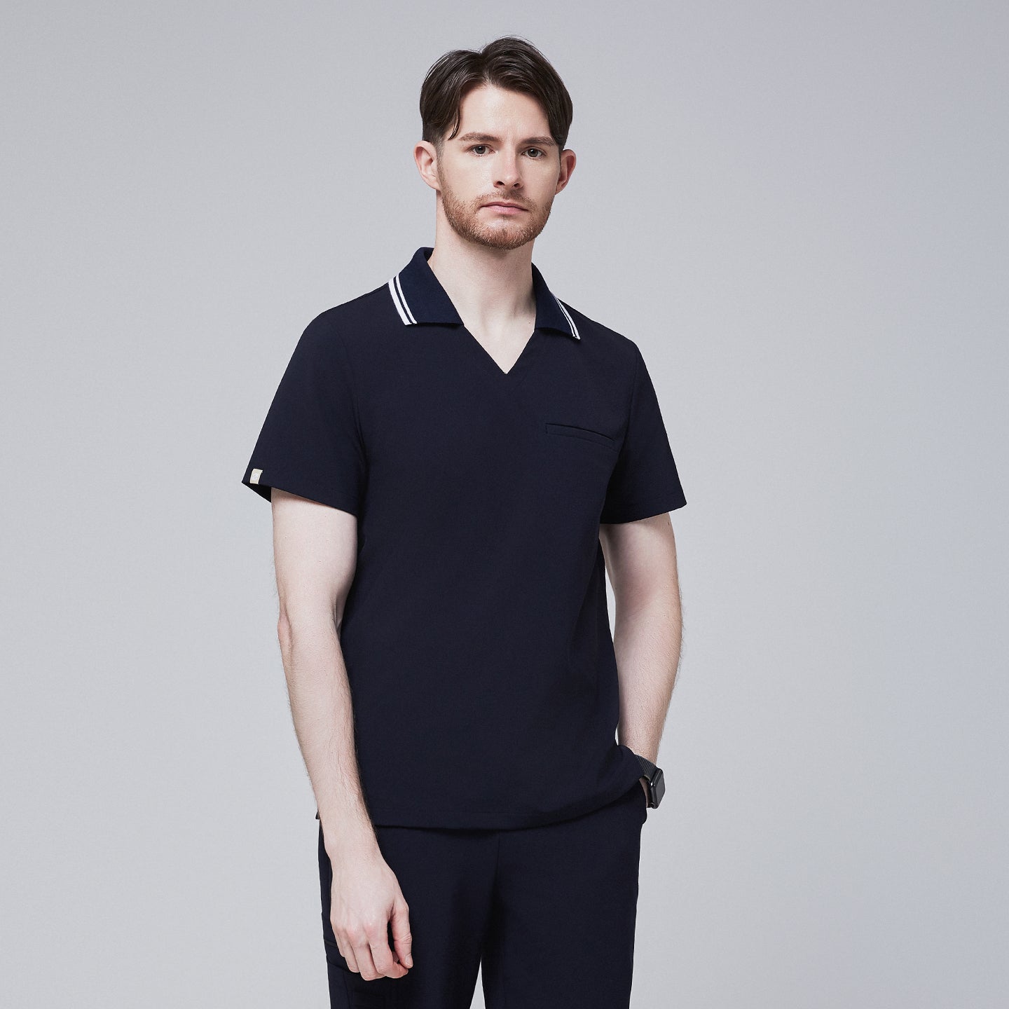 Male model wearing a midnight navy performance polo scrub top with a striped collar, standing with hands in pockets,Midnight Navy