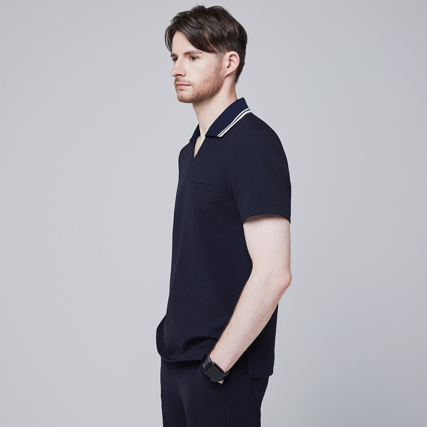 Side profile of a male model wearing a midnight navy performance polo scrub top with a striped collar and hands in pockets,Midnight Navy