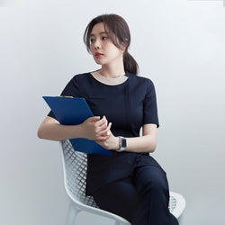 Image of  A woman in a navy round-neck front zipper top and matching pants, sitting on a white chair, holding a blue clipboard. She wears a smartwatch,Mir Navy