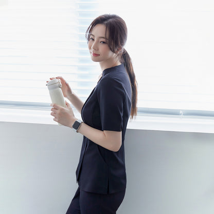 A woman in a navy round-neck front zipper top and matching pants, standing by a window, holding a white tumbler, and wearing a smartwatch,Mir Navy